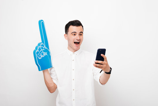 Portrait of excited young supporter, with big fan glove, wathing how hit favorite team playing online on phone