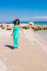 Young beautiful girl in  dress on the beach in summer. The girl in the blue sea on the sand