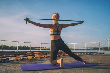 Fototapeta na wymiar Woman exercising pilates with elastic band on sunny day.
