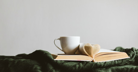 A Cup of warm drink and a book with pages folded into a heart on a cozy knitted blanket. - Powered by Adobe