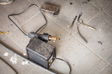Industrial soldering gun of black color on the floor among dust and tools for heating and melting plastic during the connection of parts in the workshop for repair and restoration of car bumpers
