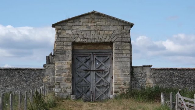 Grande porte en bois entour&eacute;e de pierres et herbes (4K HFR 60 ips) ciel bleu nuages