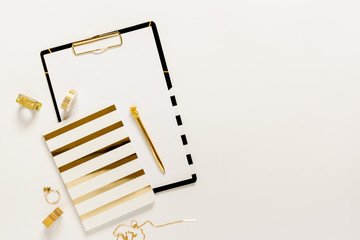 Flat lay desk table. Workspace with modern gold and black clipboard, notebook, stationery and decorations on white table. Copy space, top view