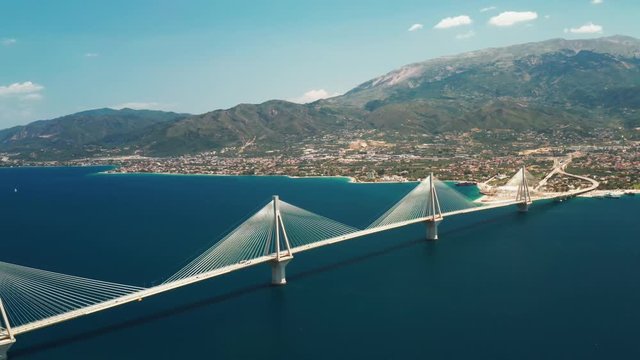 Aerial view of a drone slide turn a beautiful large bridge for the motorway across the sea in the city of Patras, Greece. Sophisticated, beautiful design of the automotive bridge in sea in the summer