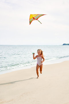 Happy Child Girl With A Kite Running On Tropical Beach