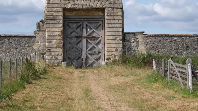 D&eacute;couverte d'une grande porte en bois entour&eacute;e de pierres et herbes (4K) pano bas haut