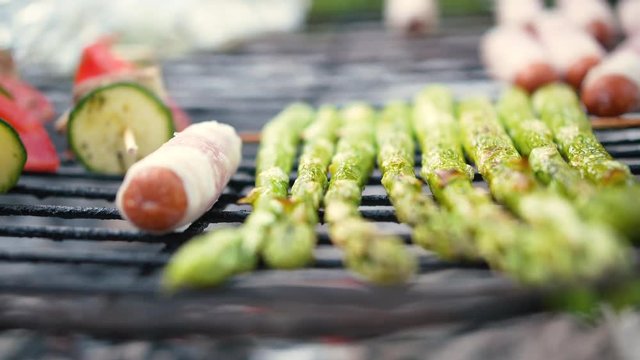Close-up shot of some asparagus, skewer and some small berner sausage on a grill.