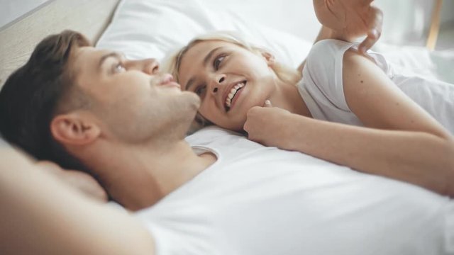 man talking and embracing beautiful laughing and smiling woman in bed