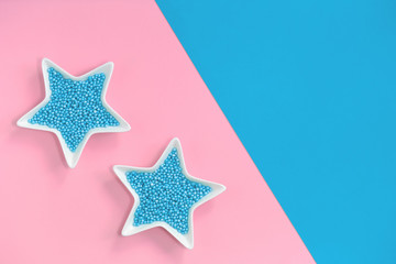 Fototapeta na wymiar Blue nonpareils cake candy sprinkles in two white star bowls on pink blue background in flat lay with copy space. Party celebration dessert menu or bakery concept