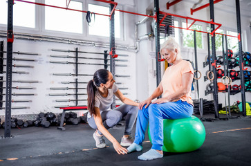Senior woman with trainer doing rehab using pilates ball in the rehabilitation center