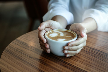 Women's hand holding a coffee cup with a heart shape