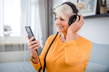 Senior woman listening her favourite music at home using headphones and smartphone