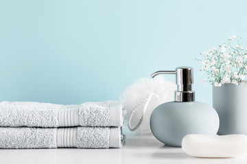 Soft light bathroom decor in pastel blue color, towel, soap dispenser, white flowers, accessories on white wood shelf. Elegant decor bathroom interior.