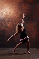 Full-length photo of dancing blonde girl looking in side in short black dress on dark brown background