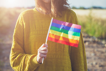 young woman wearing yellow sweater holding lgbt rainbow flag outside, same sex couples, freedom,...