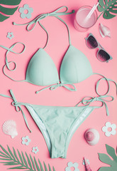 Summer holiday concept with bikini, sunglasses , sea shells and tropical leaves on pastel pink background, top view. Flat lay. Creative layout.
