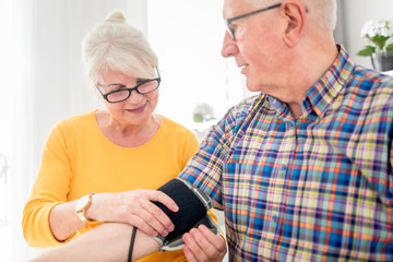 Senior wife doing blood pressure measurement at home to her husband