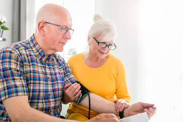 Senior wife doing blood pressure measurement at home to her husband