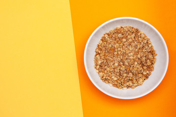 Muesli with banana in a white bowl on  orange and yellow background