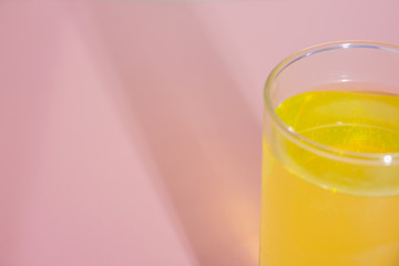 Glass with yellow liquid with shadow on a pink background