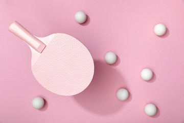 top view of white table tennis balls scattered under racket on pink background