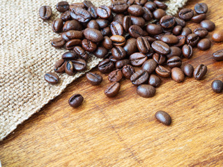 Coffee beans spilling on sackcloth and wooden table, closeup