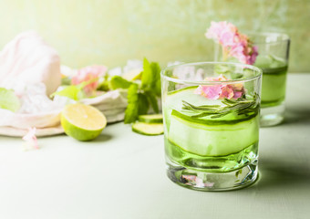 Glass with green iced cucumber lime refreshing drink on light table at wall background. Summer beverages concept. Green color . Healthy homemade lemonade with fresh herbs