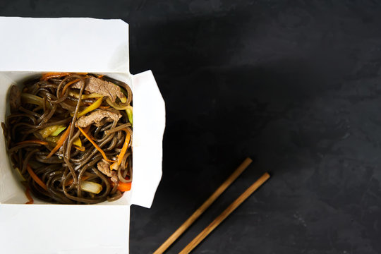 Delivery of hot lunches in boxes. Soba noodles with beef and vegetables on a black background