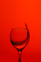 splash of water in wineglass isolated on red background.