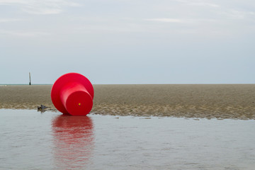 Bouée rouge sur la plage à marée basse sous un ciel gris. Côte belge
