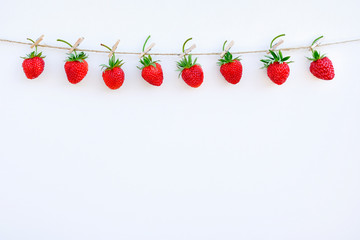 Garland of red ripe strawberries hanging on wooden clothespin on rope twine, located on top edge on...