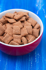 Chocolate pillows in red bowl on blue wooden background