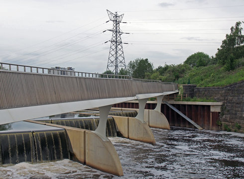 footbridge crossing the flood alleviation weir on the river aire at knostrop leeds with electricity pylons in a rural industrial landscape