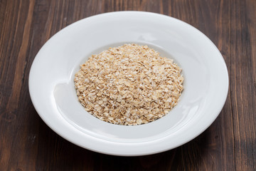 uncooked oats in white plate on wooden background