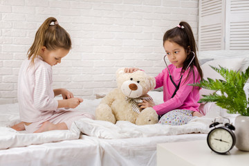 two cute children girls playing doctor with teddy bear at home. girl listens a stethoscope to toy.