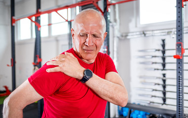 Senior man at the gym suffering from pain in shoulder