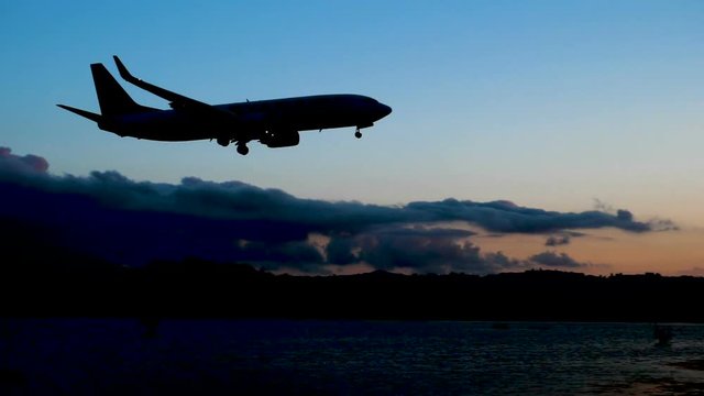 Passenger airplane flying in sky. Silhouette of aircraft landing on runway at airport of Corfu in dusk. Greece. Slow motion. HD