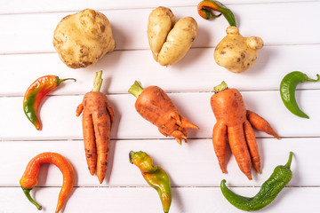 Trendy ugly curved vegetables - potato, carrot and chilli pepper on white wooden background. - obrazy, fototapety, plakaty