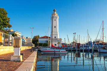 Lighthouse in sea port of Rimini, Italy. Boats moored in harbor channel in Rimini, Italy
