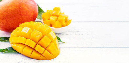 Beautiful chopped mango chunks with green leaves on bright white color timber background. Copy...