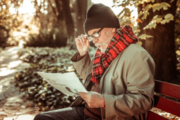 Concentrated aged man attentively reading a newspaper.