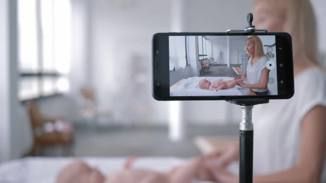 maternal care, blogger mom teaches how to change a diaper child girl lying on a changing table while recording training video on mobile phone