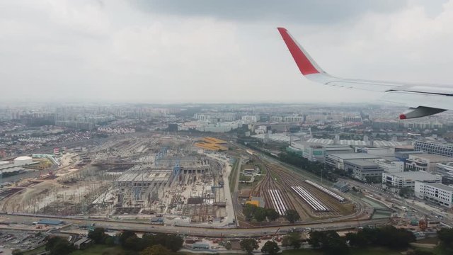 Aircraft on approach to Denpasar, Bali airport flying low over the city on a cloudy afternoon. View through plane window of wing tip and landscape below.