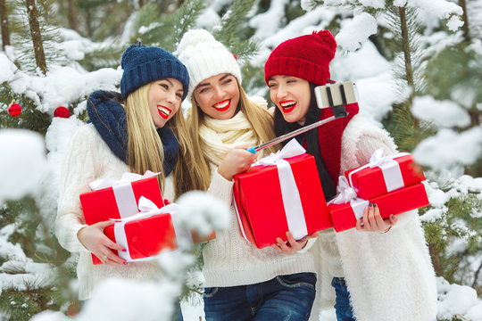 Group of young girls makin selfie with christmas presents outdoors. Cheerful friends making a picture on the mobile camera