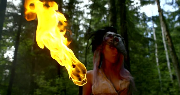 wild female magician is wearing skull of big bird is holding torch in hand in woodland