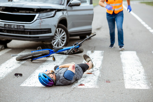 Road accident with injured cyclist lying on the pedestrian crossing near the broken bicycle and car driver running on the background