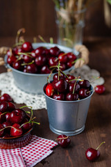 Composition with ripe cherries in metal bowls and clay brown plate. Vintage napkins as decor. Dacha style, countryside, cozy and cute, grandmother's kitchen
