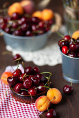 Ripe apricots and cherries in metal bowls and clay brown plate. Vintage napkins as decor. Dacha style, countryside, cozy and cute, grandmother's kitchen. Dry flowers in vase on background