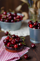 Composition with ripe cherries in metal bowls and clay brown plate. Vintage napkins as decor. Dacha style, countryside, cozy and cute, grandmother's kitchen