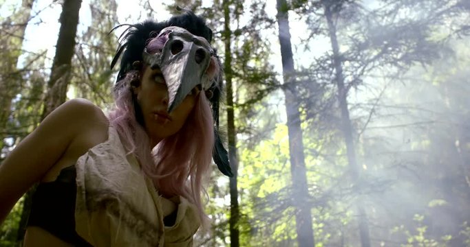 actress is acting wild ancient shaman with bird skull on head in woodland in summer day